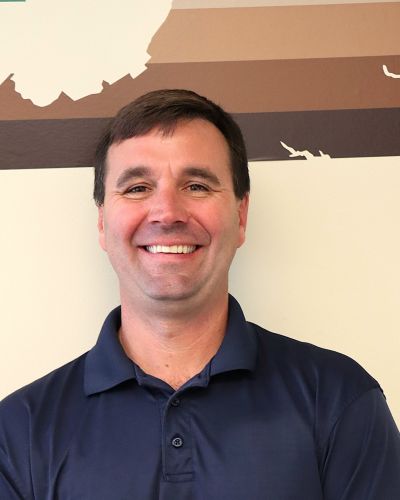 Smiling man in blue shirt standing in front of map of virginia